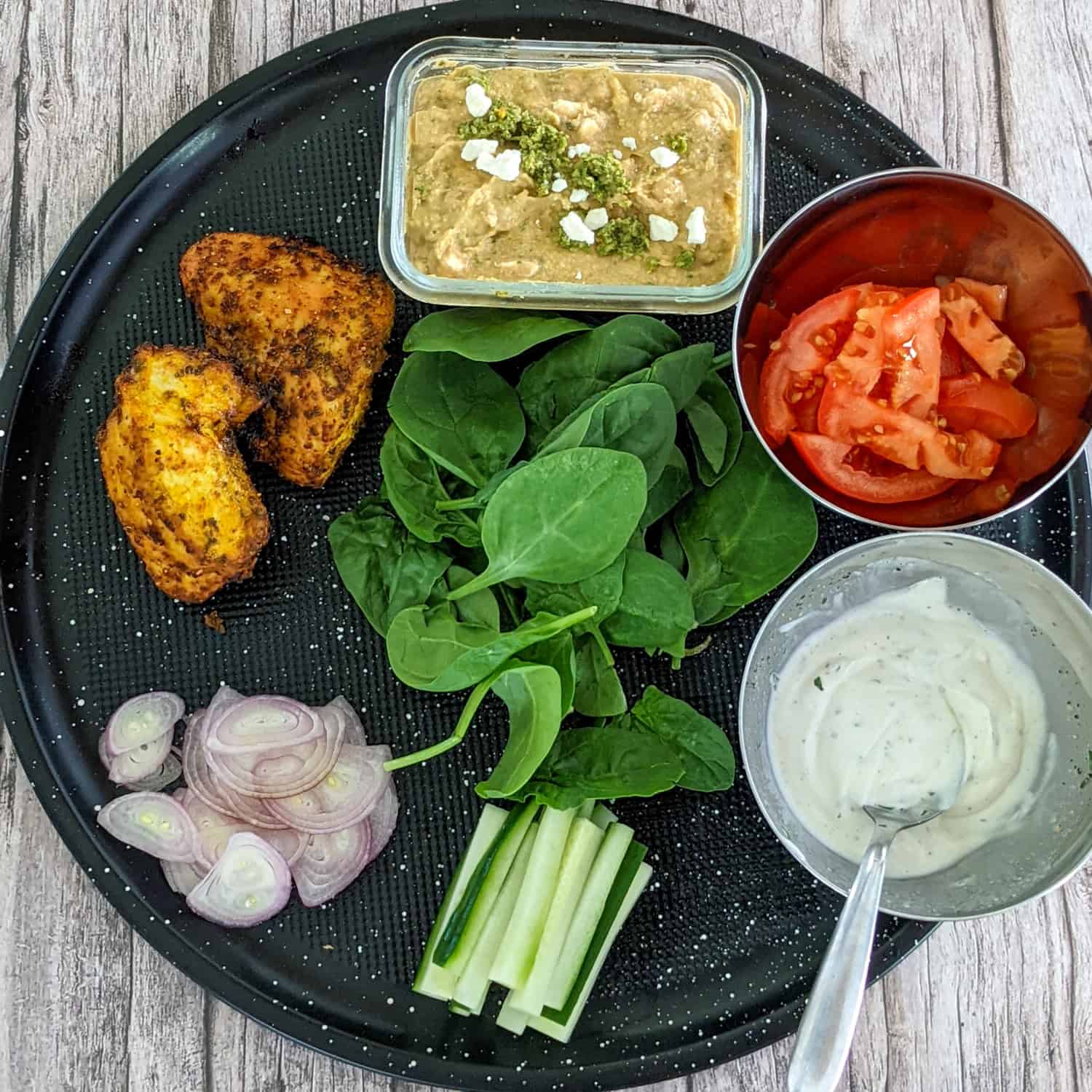 prepped ingredients for the zhug feta hummus chicken wrap on a round black pizza pan
